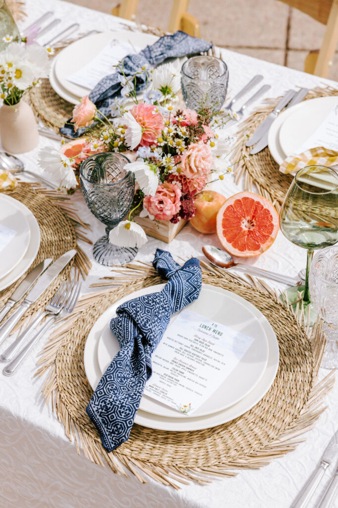 Outdoor wedding reception at The Little Nell in Aspen, Colorado. Table lined with white linens, straw charger mats, blue napkins, and fresh fruit.