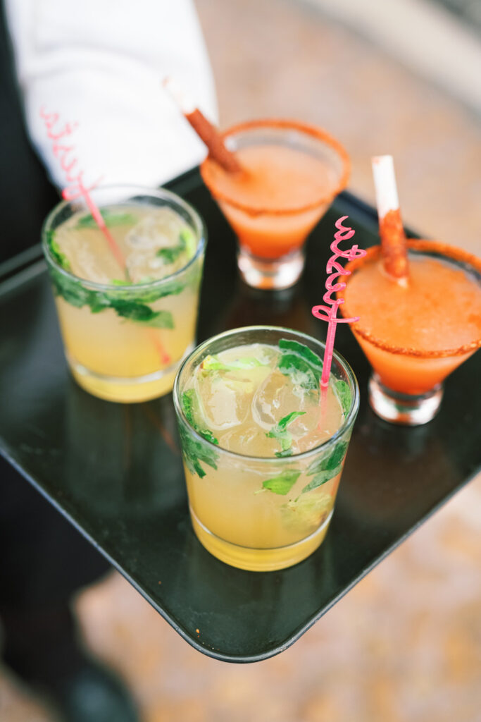 Waiter holding a tray with a selection of vibrant mixed drinks, including mojitos and a margarita, garnished with fresh herbs and colorful straws, ready to be served at a social event in San Miguel, Mexico.