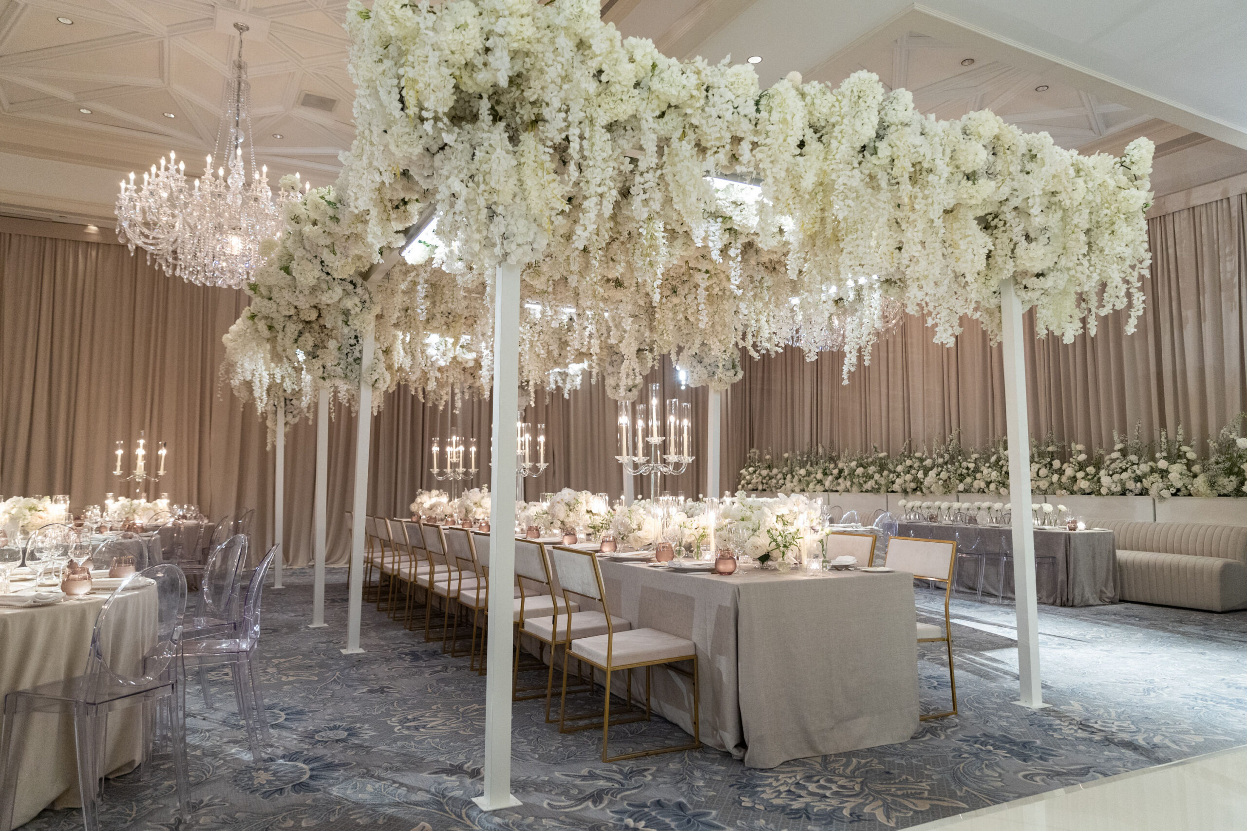 Details of a venue transformation in Dallas, with large floral arrangements hanging from pillars above the tables, with all white flowers