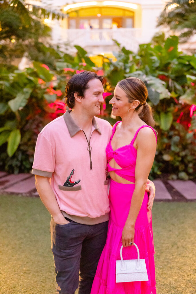 A couple in vibrant formal wear shares a loving gaze amidst a backdrop of tropical greenery, radiating joy and color.