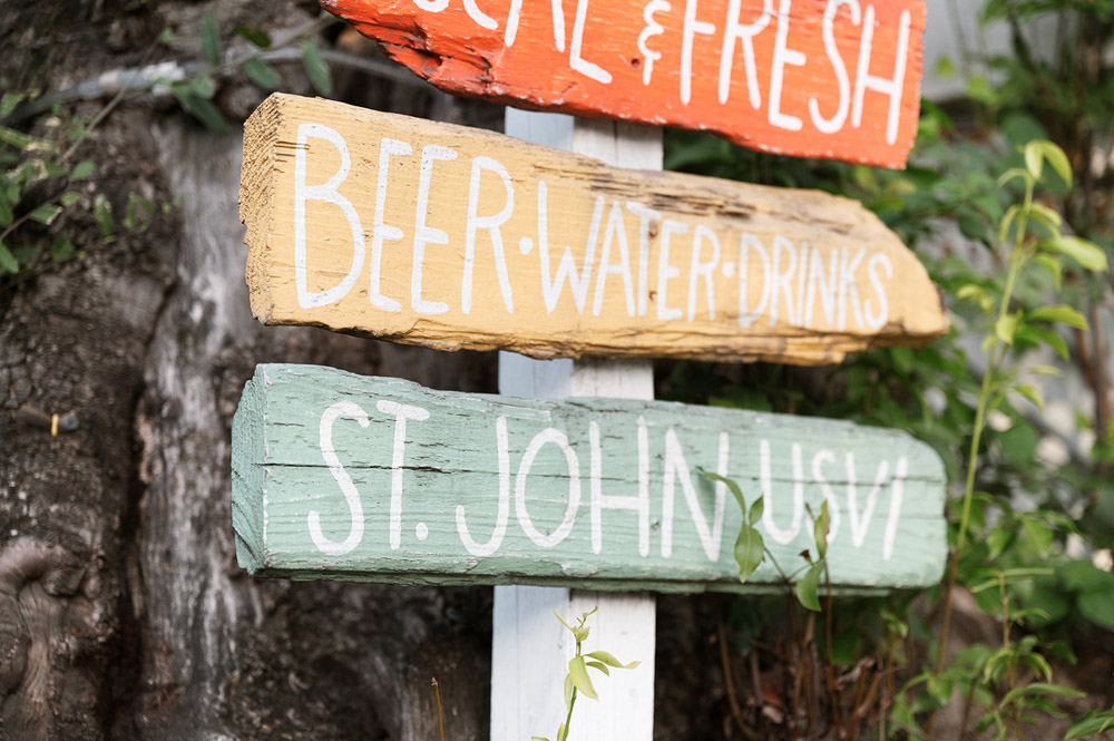 Close-up of a colorful signpost with hand-painted directions in pastel hues, against the natural backdrop of St. John, USVI.