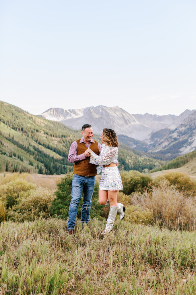 Caught in a moment of joy, the couple dances in an open field, the grandeur of the Rocky Mountains in Aspen providing an epic backdrop. Her flowing dress and his casual cowboy attire blend perfectly with the natural majesty around them.