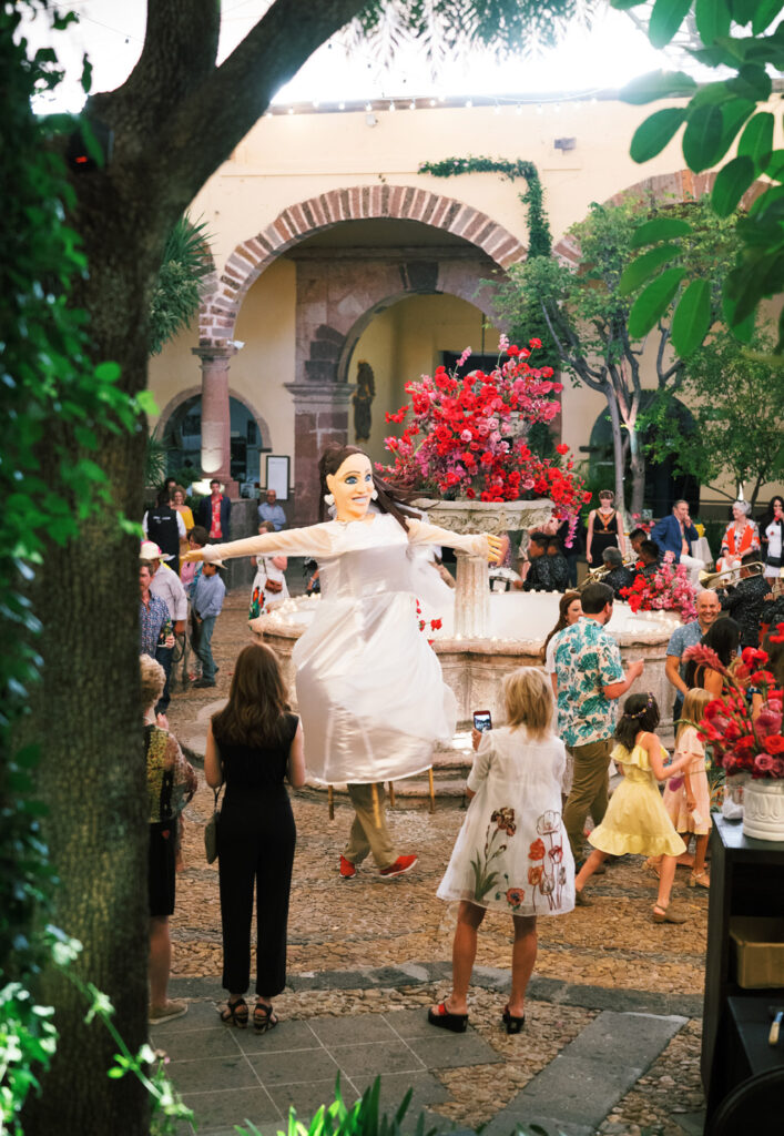 festive event in a courtyard adorned with flowers and arches, surrounded by spectators capturing the moment.