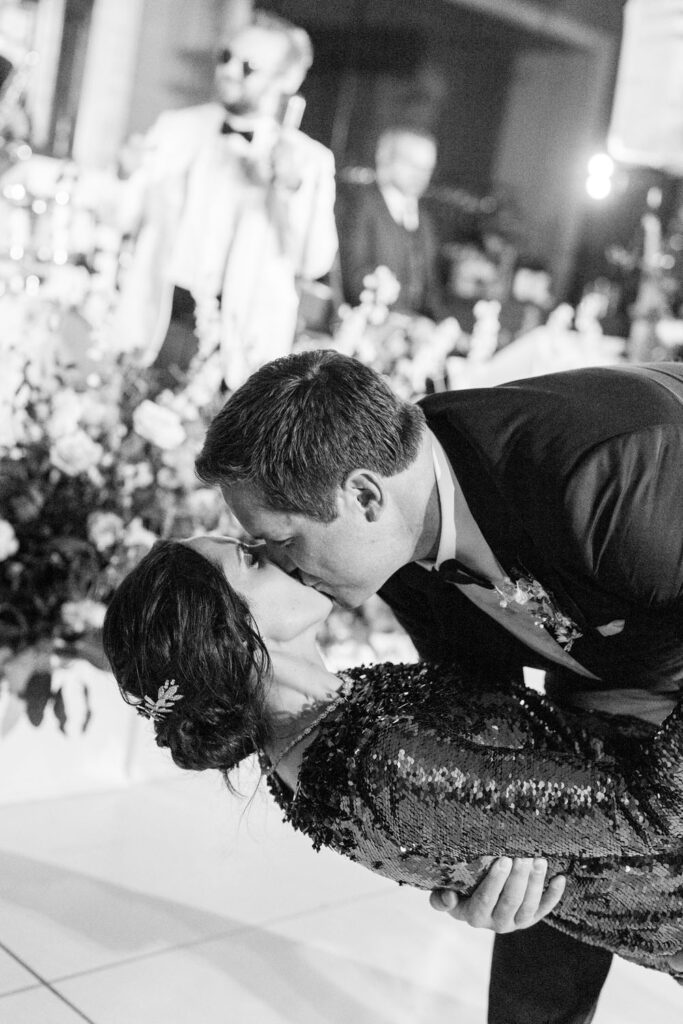 Groom dipping the bride for a dramatic kiss on the dance floor, captured in a timeless black and white shot.
