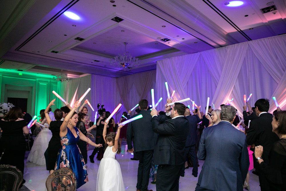 Wedding reception dance floor alive with guests waving multicolored glow sticks, creating a vibrant and festive atmosphere.