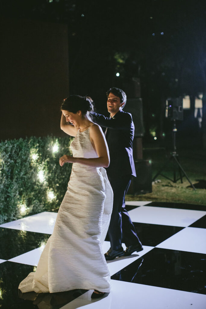Bride and groom share an intimate dance on a checkered dance floor under the night sky, illuminated by surrounding twinkling lights.