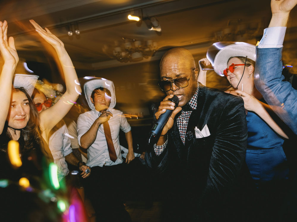 Dynamic singer in a velvet jacket performing amidst a lively crowd on the dance floor, with a blurred motion effect capturing the energy of the moment.