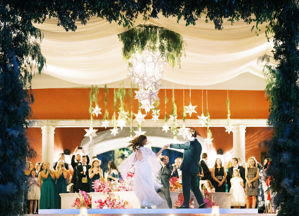 Bride and groom dancing energetically under white draped linen and hanging star lights at the Rosewood Hotel venue in San Miguel, surrounded by guests and floral decorations, capturing a moment of celebration.