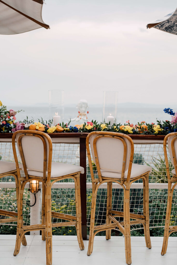 Wooden chairs overlooking the water in Capri, Italy with colorful flowers on a table