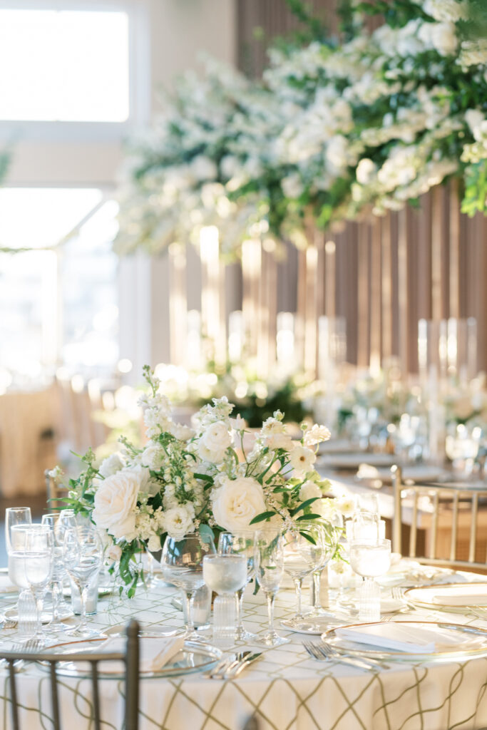 Sunlit wedding reception with white and gold linens, and large flower arrangements with all white flowers. Inside of Current in NYC