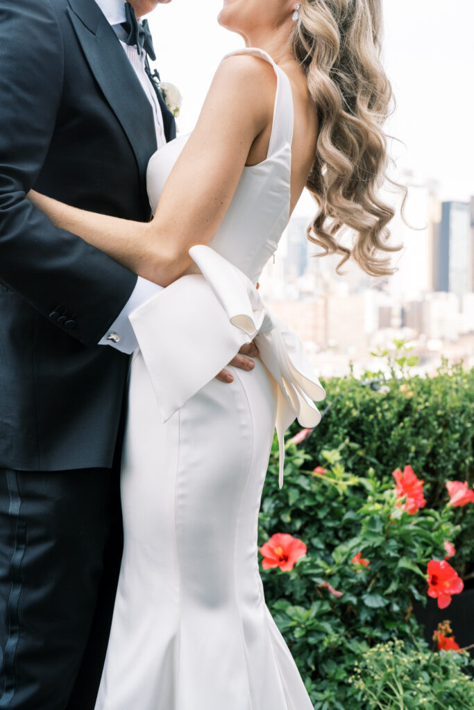 A detail closeup of a bride and groom embracing, on a patio overlooking the NYC skyline