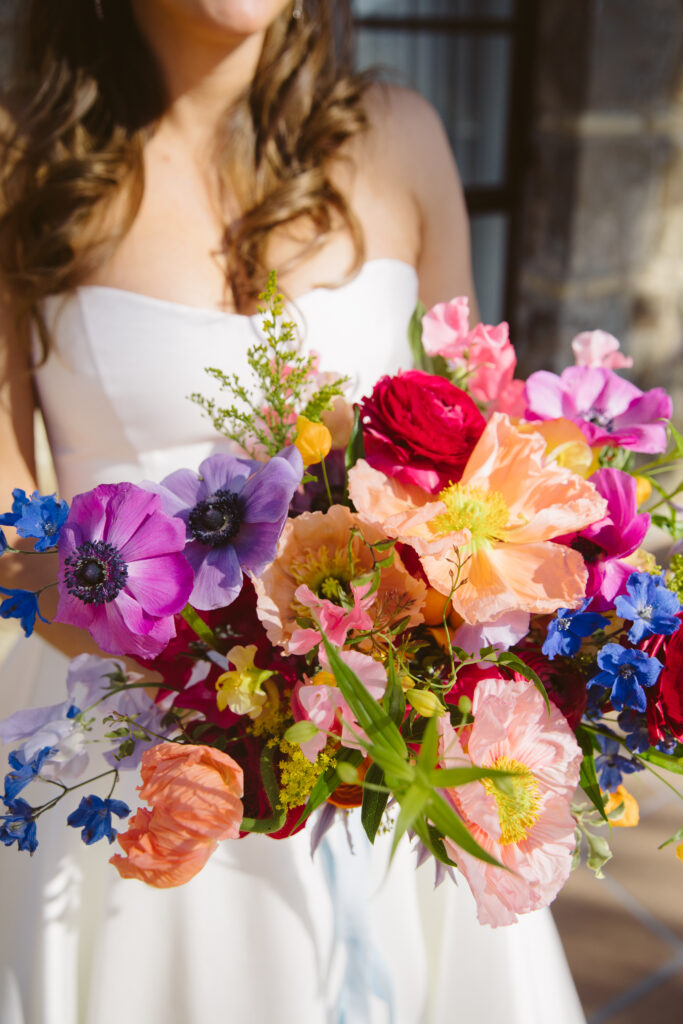 Bride holding a multi-colored bouquet with anemones, peonies, ranunculus, and poppies.