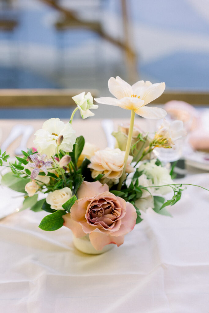 Mauve garden rose, white anemones in a small centerpiece on a table at a wedding reception.