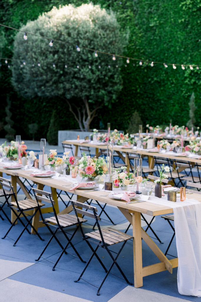 Long wooden tables with white runners and vases of flowers, under cafe lights, at a wedding reception at The Fig House