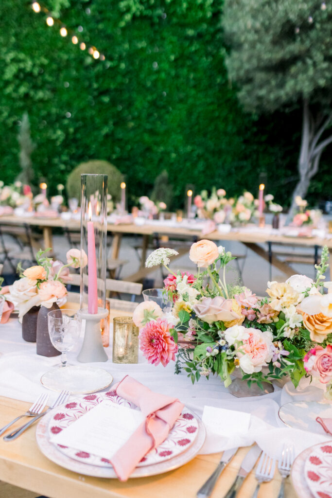 Pink floral plates with blush pink napkins sitting on a wooden table, for a wedding reception outdoors