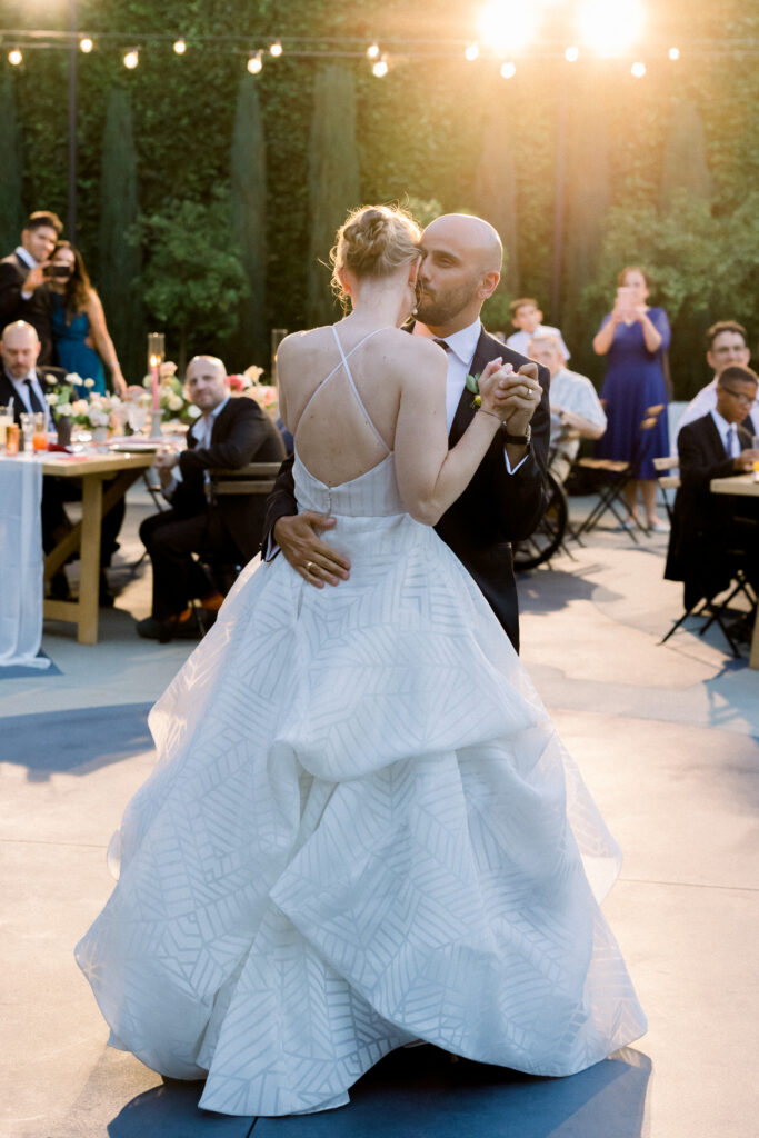 Bride and groom first dance at sunset outside under cafe lights at The Fig House